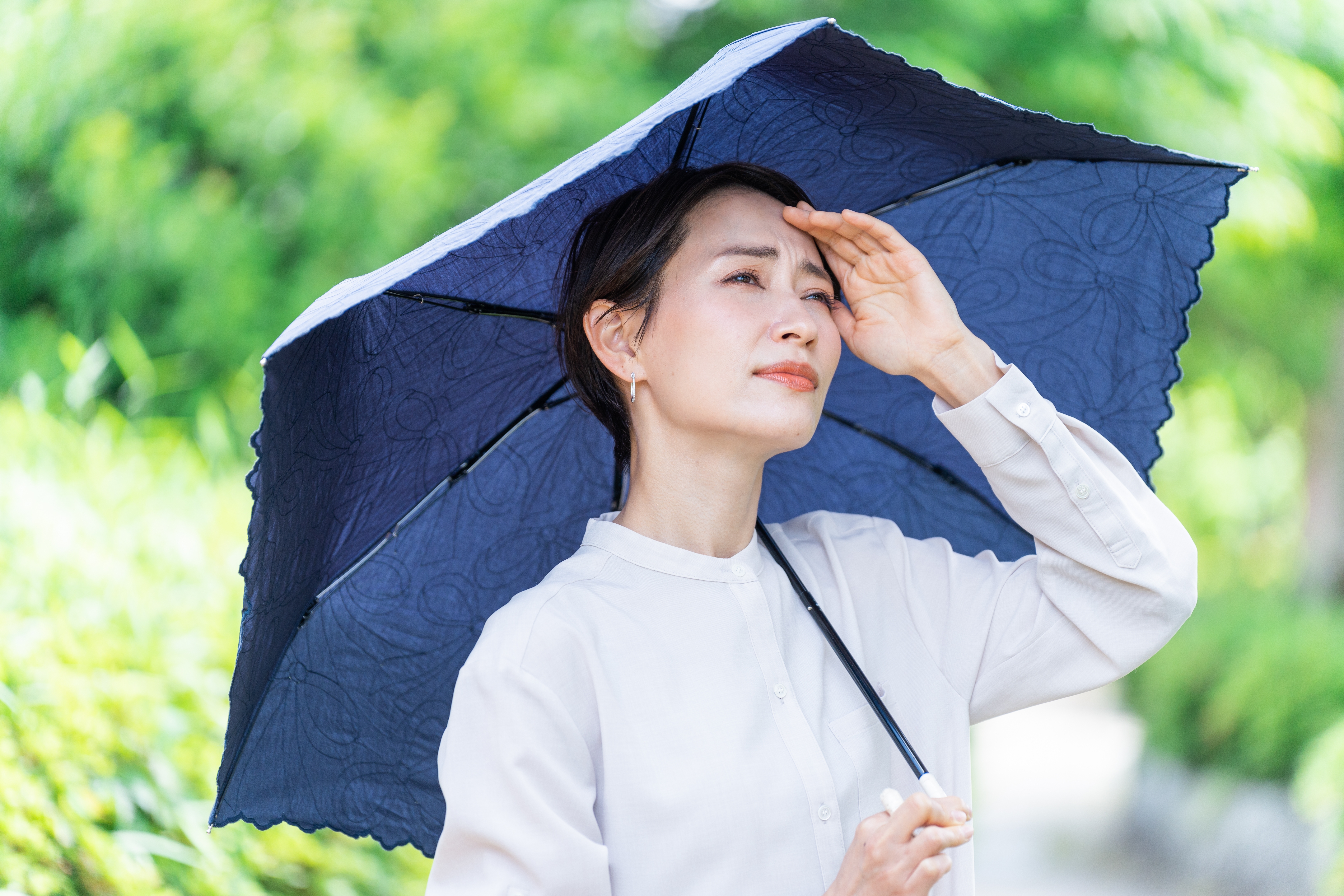 An Asian woman standing outside, shielding herself from the hot sun with an umbrella