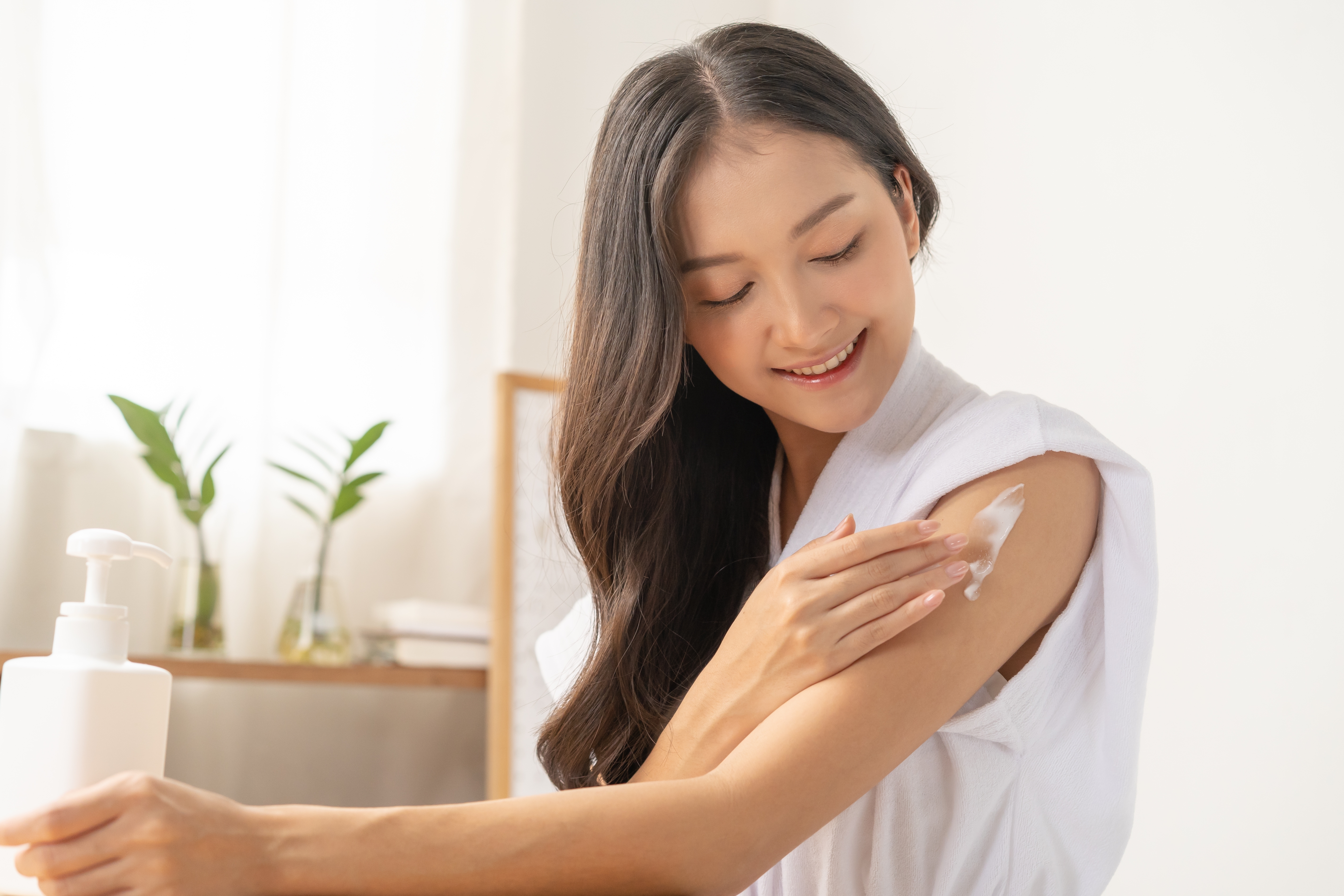 An Asian woman applying lotion on her arm indoors